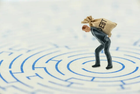 Figurine of a businessman hunched over with a sack saying 'debt' on his back in the centre of a maze