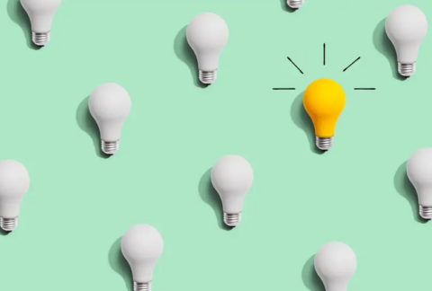 Cartoon of lightbulbs arranged in linear pattern, all switched off apart from one that is yellow with glow lines drawn around it