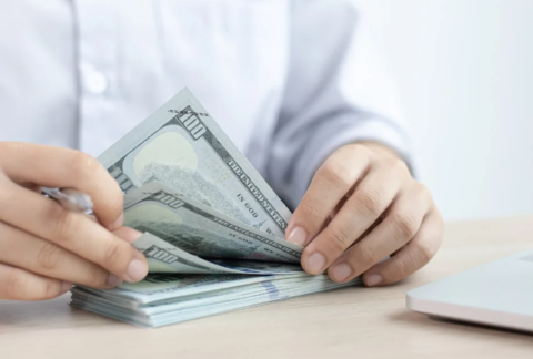 Businessman leafing through wad of cash at desk