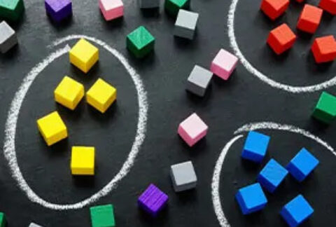 Three circles drawn on a chalk board, one with yellow wooden cubes inside, one with blue, and one with red, and cubes of different colours scattered outside the circles