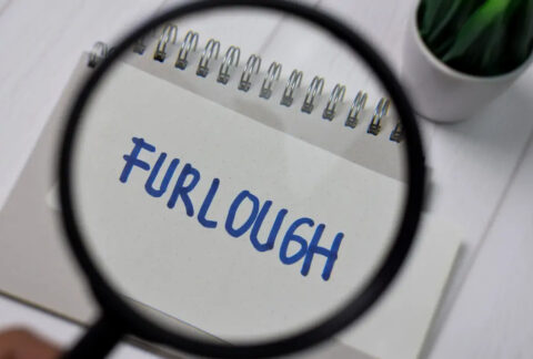 Magnifying glass held over piece of paper with 'furlough' written on it