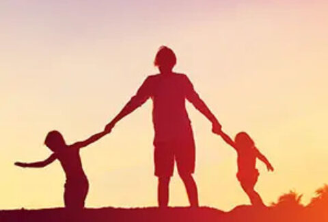 Silhouettes of a parent holding hands with two children against sunset
