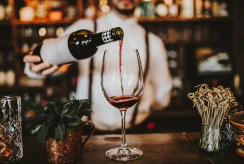 Bartender pouring red wone from bottle into glass