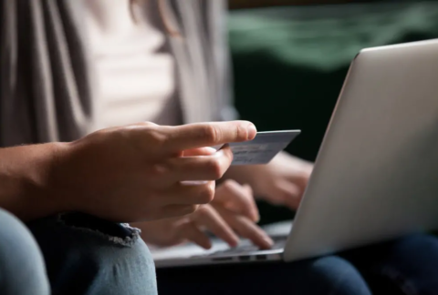 Man sitting down with bank card in hand in front of woman sitting with laptop