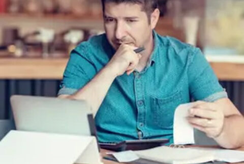 SME owner making calculations with receipts, tablet and calculator at table in cafe