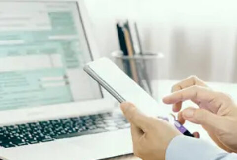 Businessman using smartphone at desk in front of open laptop