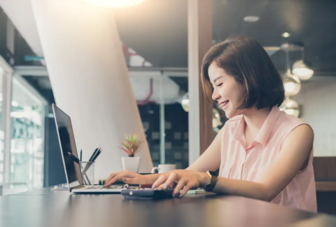 Businesswoman at desk using laptop with one hand and calculator with the other to work out personal allowance