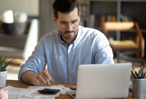 Businessperson sitting at desk looking at laptop and using calculator