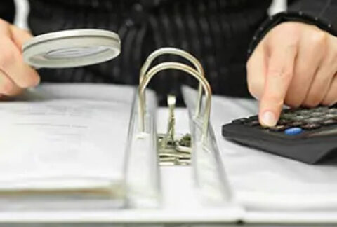 Investigator holding magnifying glass in one hand and using calculator with the other on top of an open ring binder