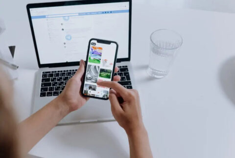 Person using a smartphone at desk in front of an open laptop