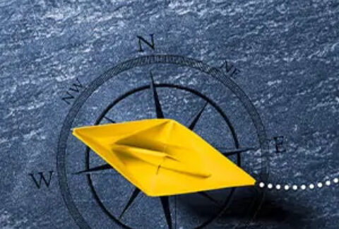 Model boat made from yellow paper on top of a compass face background with a dotted trail behind it