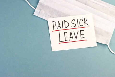 Piece of paper with 'paid sick leave' written on it on top of face mask