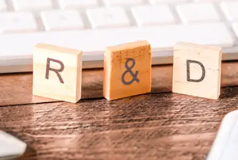 Wooden scrabble-style tiles balanced upright in front of computer keyboard spelling out R&D