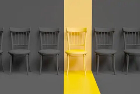 Row of chairs in dull grey lighting with a chair in the middle lit up with gold lighting