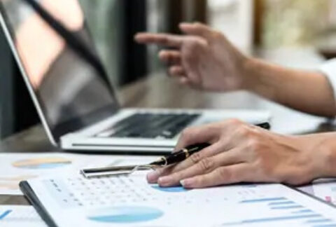 Businessman working on laptop and looking at documents showing graphs and charts