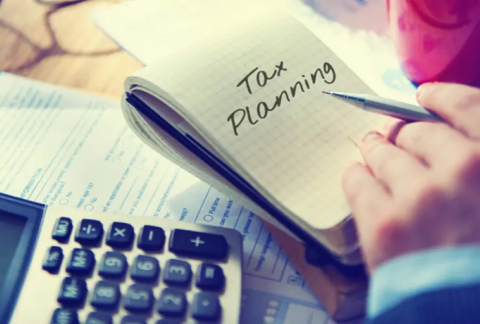 Hand holding pen over open notebook with 'tax planning' written on page