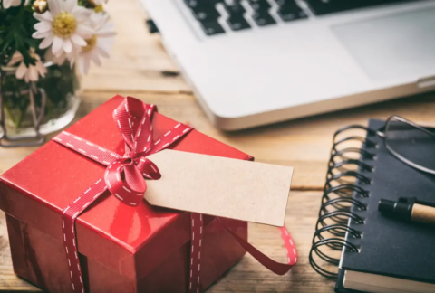 Small Christmas gift on wooden desk next to notebook and laptop