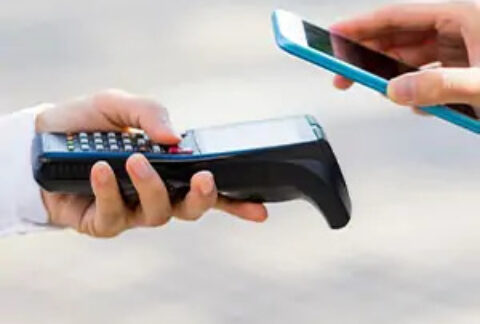 A hand holding a card machine and a hand holding a phone above it to make a contactless payment