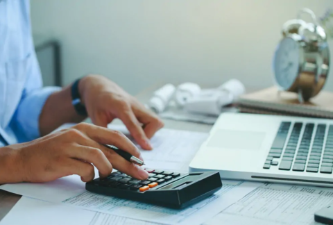 Businessperson at desk using calculator with one hand and pointing at tax return document with the other