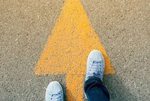 Two feet standing on a yellow arrow painted on the road pointing forwards