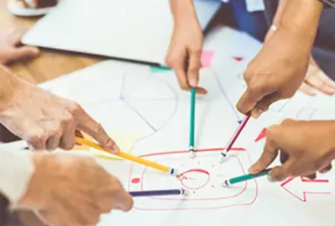 Businesspeople pointing at same point on business goals diagram with pencils