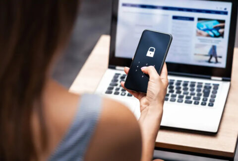 Woman entering passcode to unlock smartphone in front of open laptop