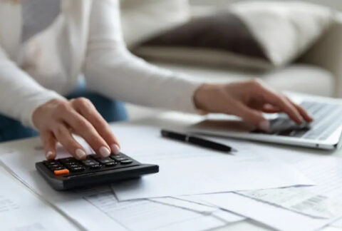 Businesswoman using calculator with one hand and laptop with the other