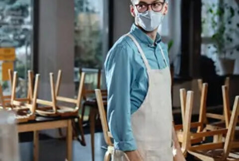 Waiter wearing facemask standing in closed restaurant