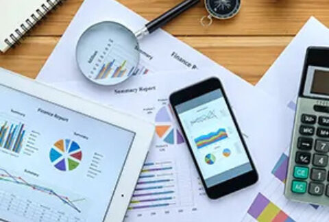 A tablet, smartphone and papers showing graphs on desk with a magnifying class and calculator