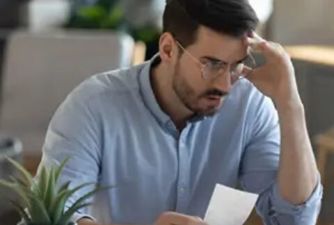 Businessman with hand to forehead holding a document at desk
