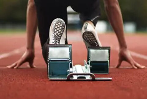 Runner kneeling at starting blocks of racetrack from behind