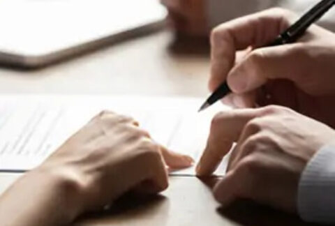 Two hands pointing at document on table and one hand holding a pen over it
