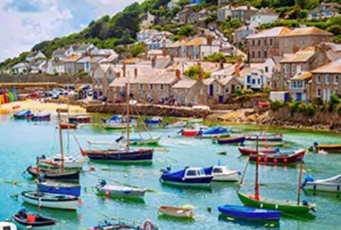 Sailboats in a sunny harbour by a beach with houses on a hill