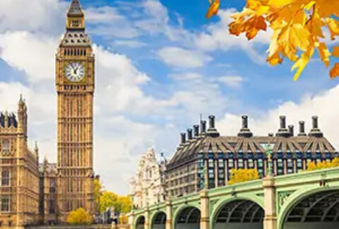 Big Ben and London Bridge against a blue sky and clouds with autumnal orange leaves in foreground