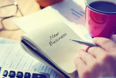 Businessman holding pen over open notebook with 'new business' written on the page