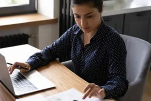 Businesswoman using calculator with one hand and laptop with the other