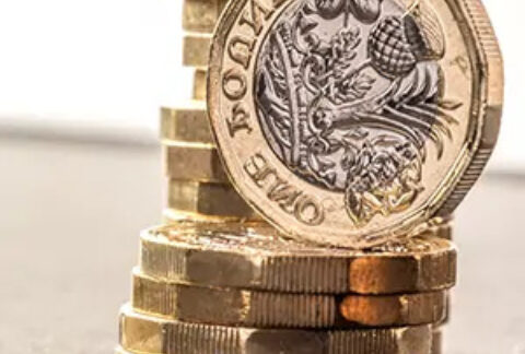 A taller stack of pound coins behind a shorter stack with an upright pound coin balanced on top