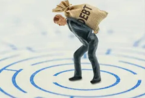 Figurine of a businessman hunched over with a sack saying 'debt' on his back in the centre of a maze