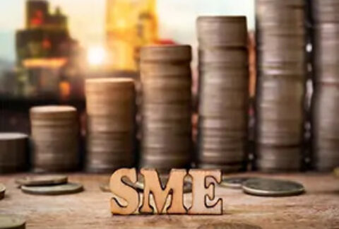 3D metal letters spelling out SME in front of increasingly tall stacks of coins with a city skyline in the backgrouns