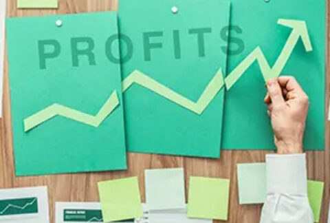 Businessman's hand holding an arrow showing increase over sheets of paper on a noticeboard with the word 'profits' across them