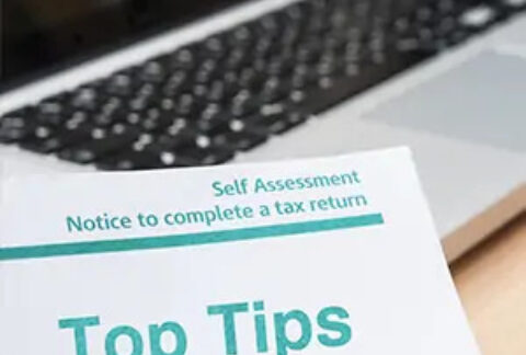 Sheet of paper with 'Self Assessment notice to complete a tax return' header and 'top tips' beneath, in front of an open laptop