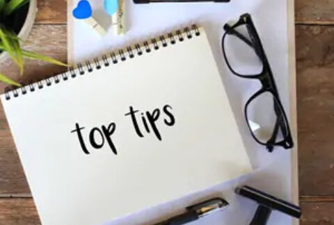 Open notebook with 'top tips' written on page on top of clipboard on desk