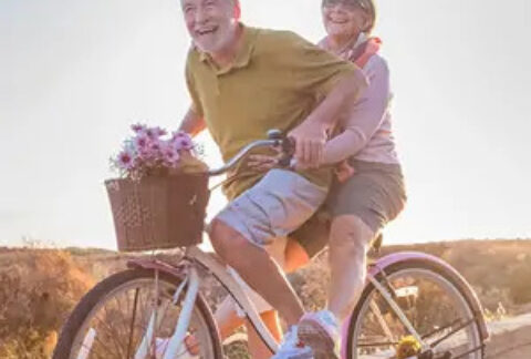 Elderly couple riding tandem bicycle in countryside and smiling