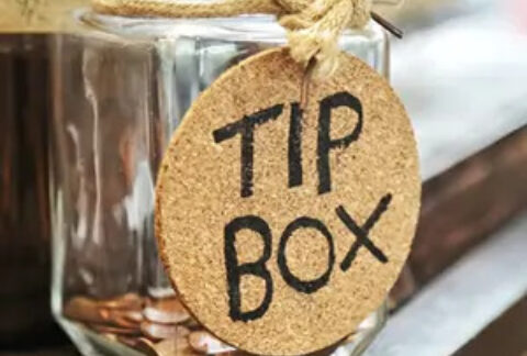 Jar with some coins inside on a ledge with a 'tip box' tag hanging from the rim