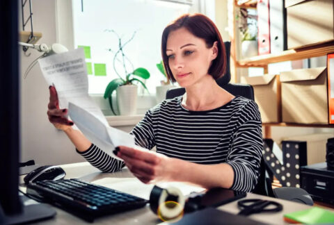 Businesswoman working from home reading letter in front of desktop