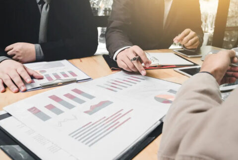 Businessmen in meeting pointing at documents displaying graphs and charts