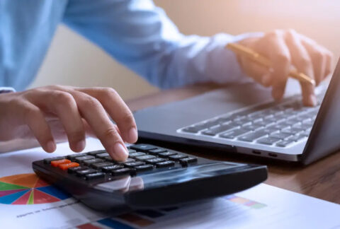 Businessperson using calculator with one hand and laptop with the other