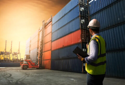 Man wearing high-vis and hard hat instructing loading of containers to cargo ship