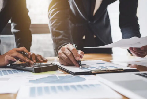 Two businessmen standing at desk looking at documents and making Corporation Tax calculations