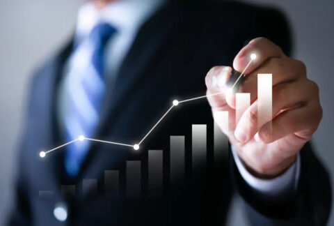 Businessman holding pen at plot point of image of an increasing line graph above an increasing bar chart